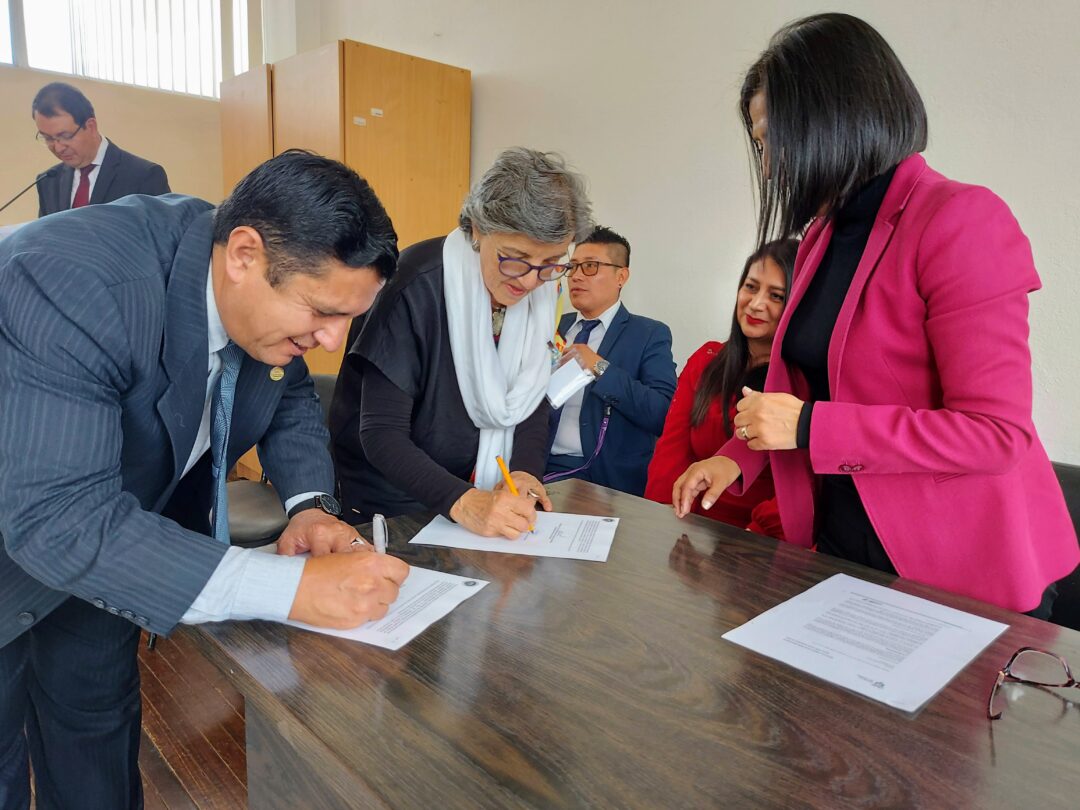 Dos personas firman un convenio de cooperación en una mesa en la Facultad de Ciencias Sociales de la Universidad Central del Ecuador.