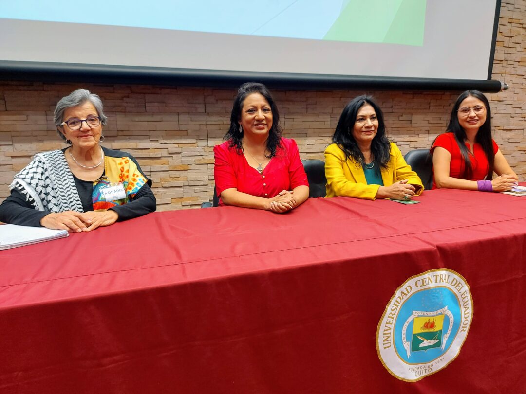 Cuatro mujeres en una mesa con mantel rojo en un evento sobre Violencia de género en la educación superior en la Universidad Central del Ecuador.